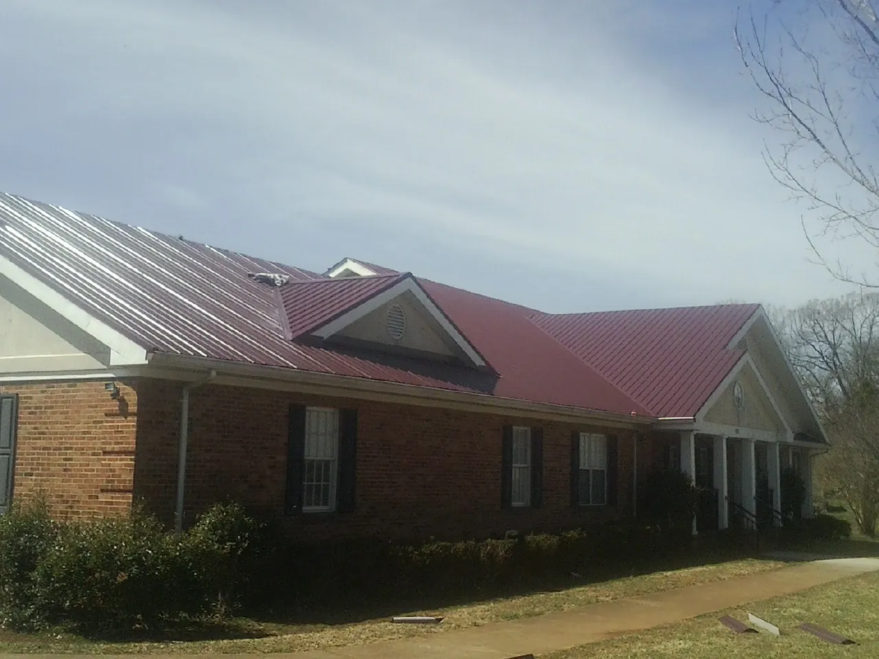 Red metal roof with gabled entries on a long brick building, from a Hail Damage Roof Repair job in Altamonte Springs