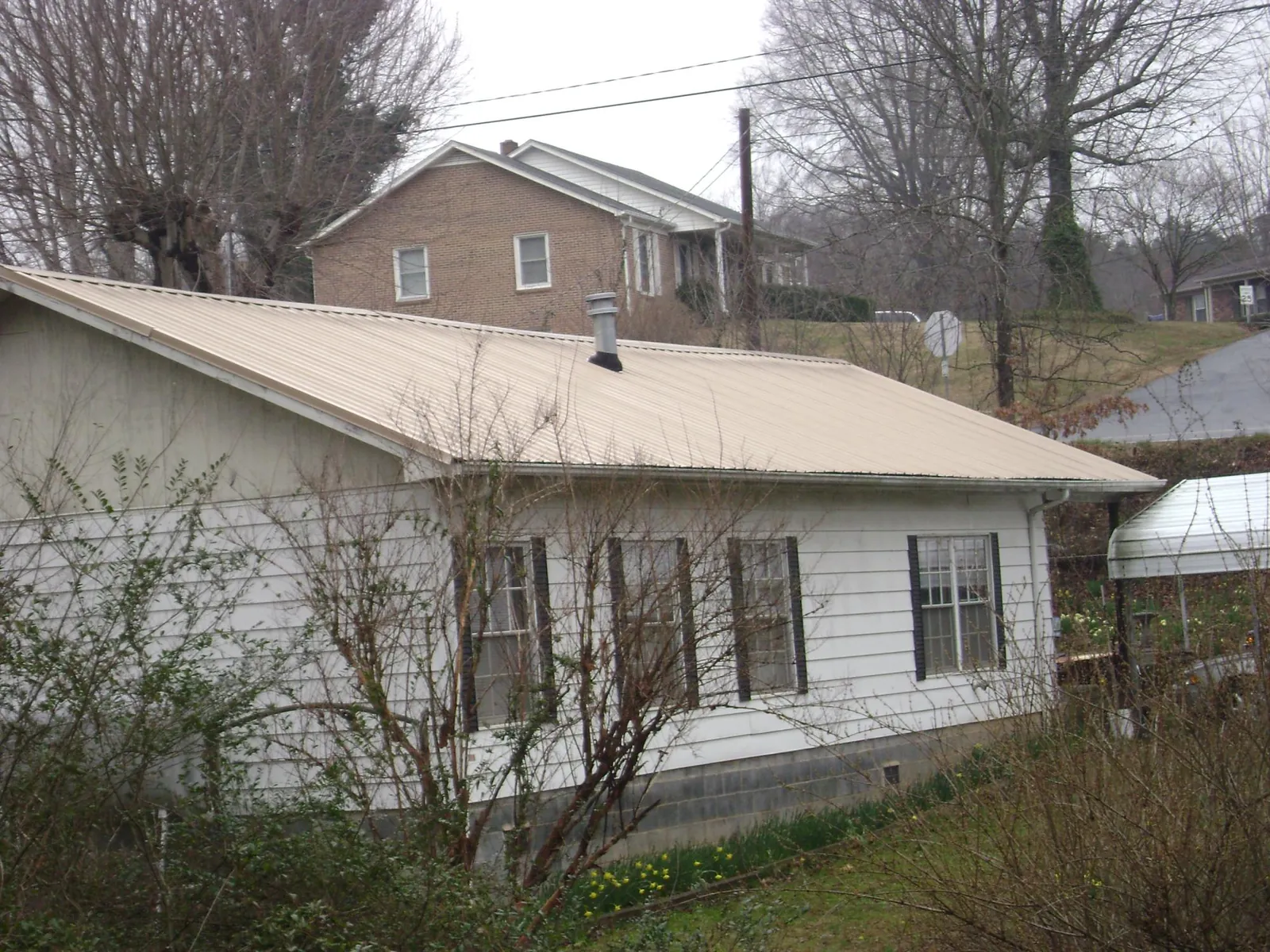 Tan metal roof on a white sided house set into a hillside — Commercial Roofing by Roofing Brothers in Altamonte Springs